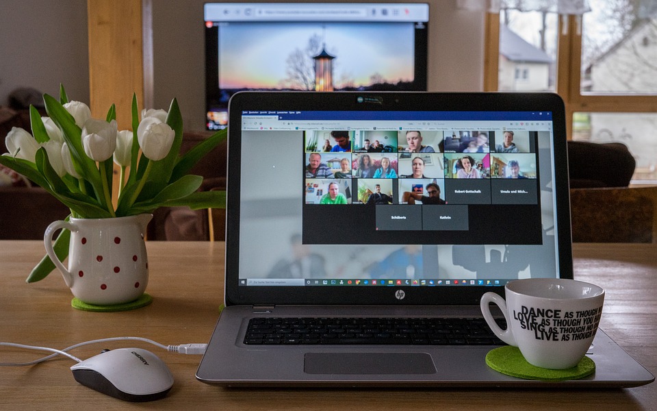Laptop displaying virtual conference call next to flowers and a coffee cup.