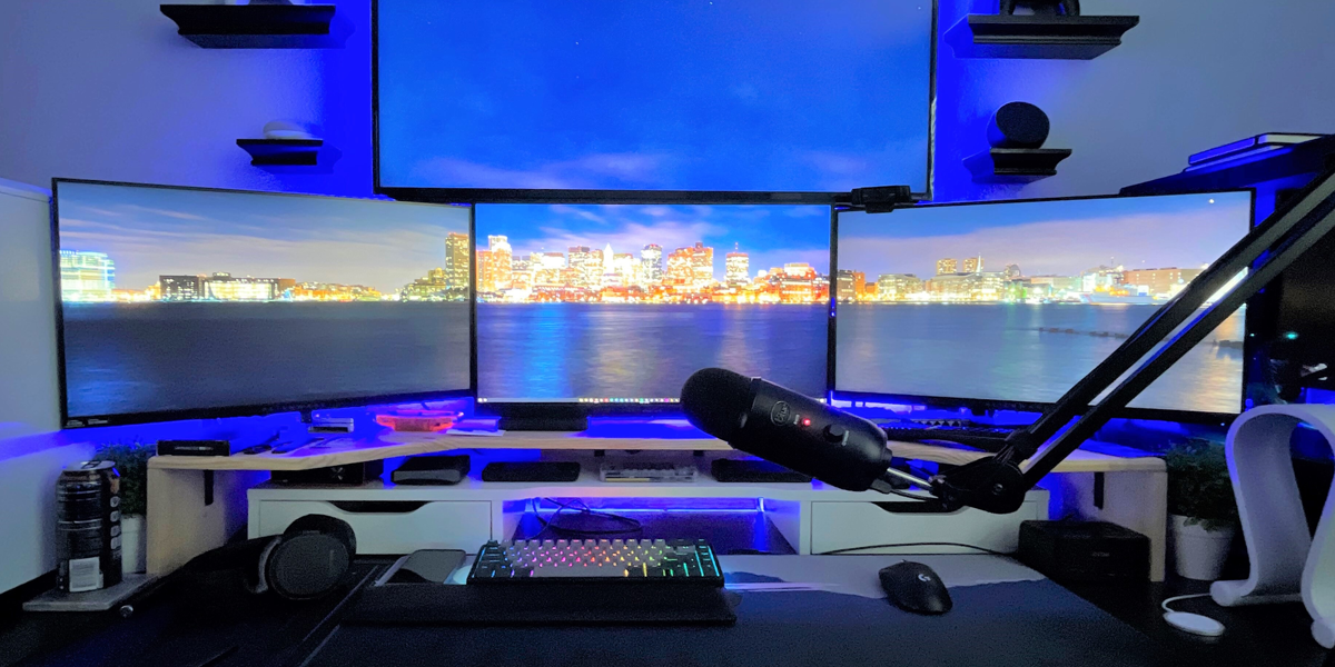 Home work station with multiple monitors, light-up keyboard, and microphone.