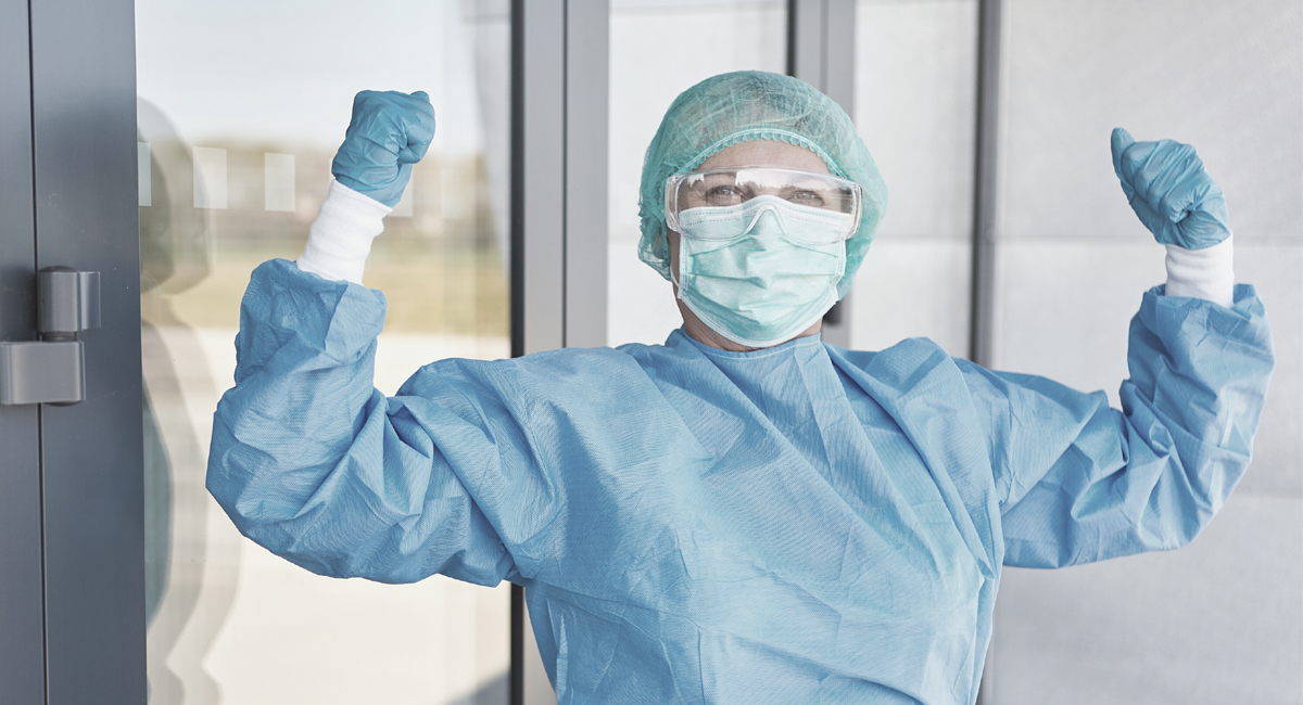 Medical professional wearing scrubs and mask with her fists raised triumphantly.