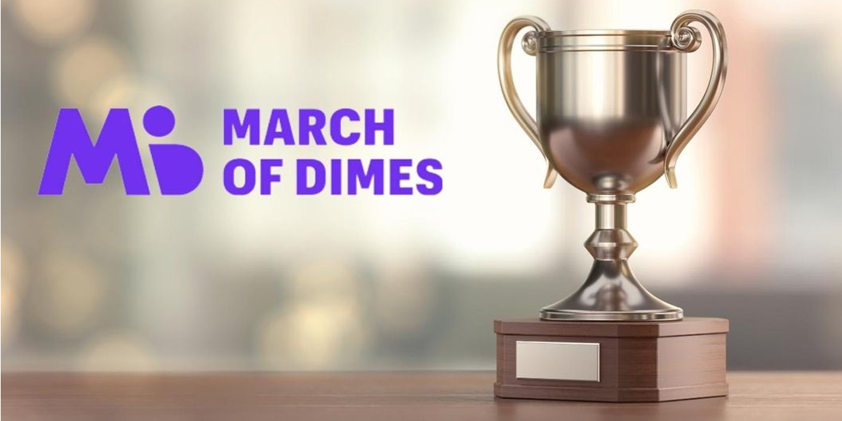 A gold trophy with wooden base on a table with the words "March of Dimes" in purple text.