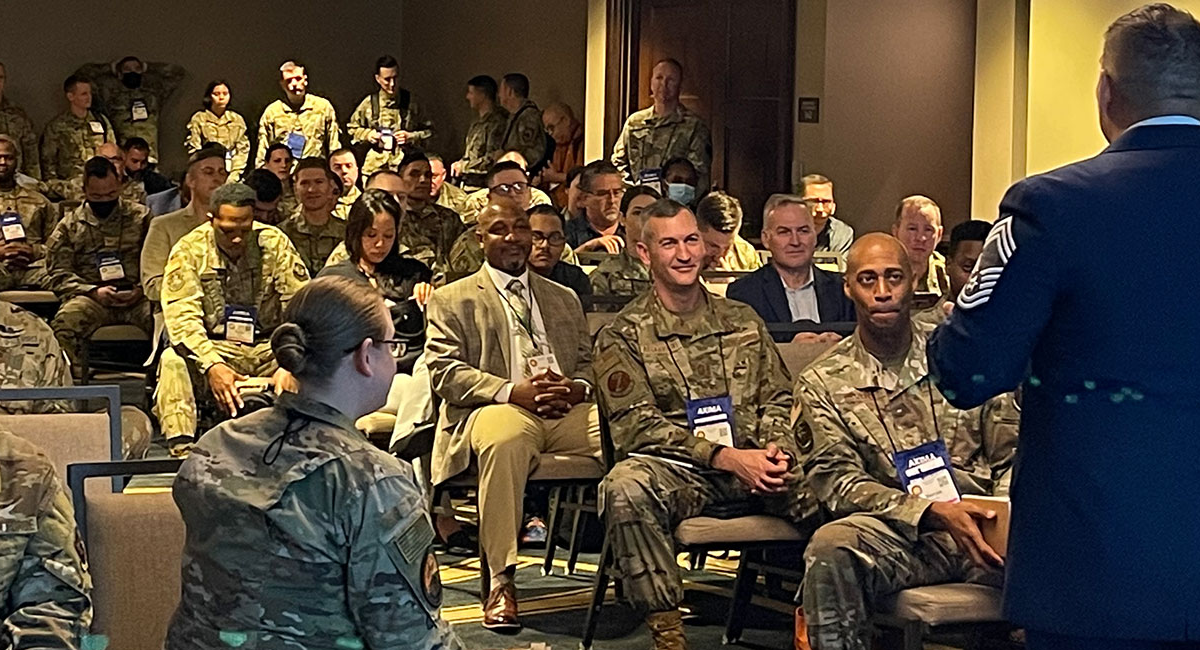 An audience of conference members in military uniforms.